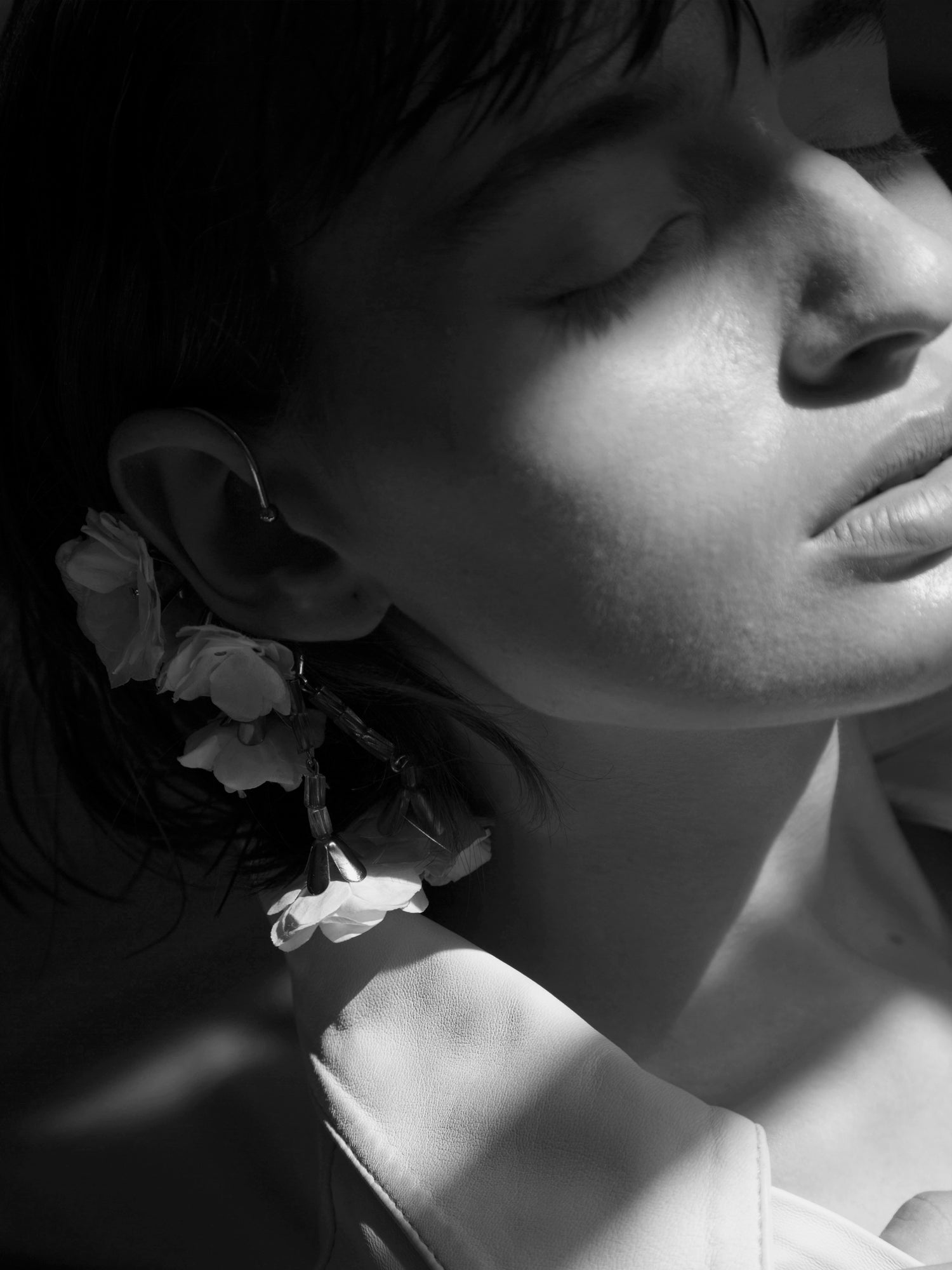 Imagen de mujer de perfil, con un rayo de sol pegando en su cara, con unos pendientes de flores.