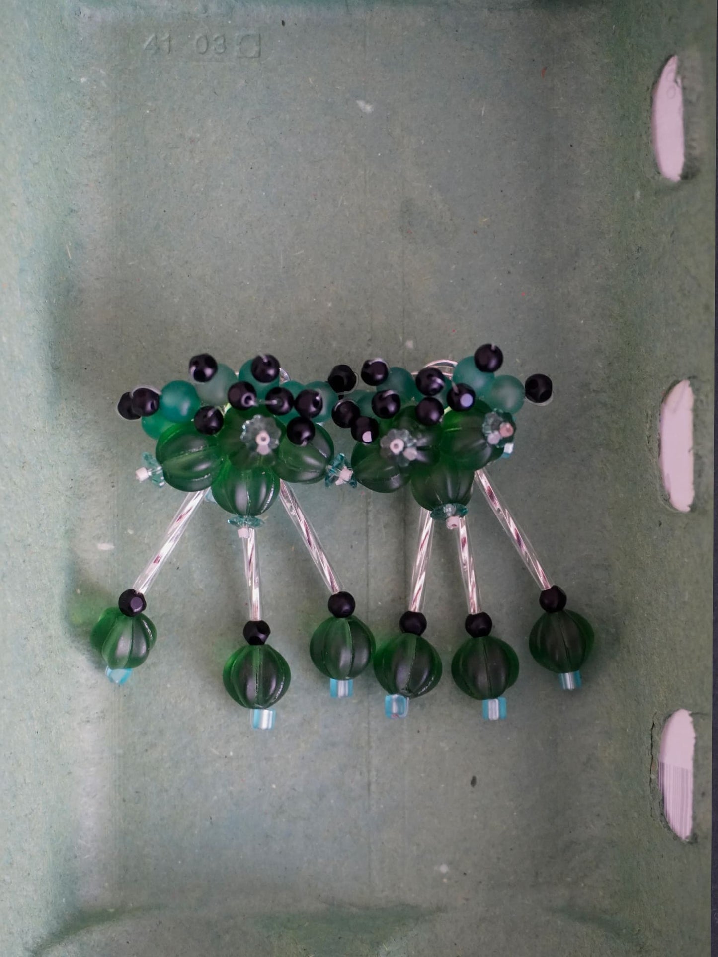 Pendientes bordados verde con diseño floral y cuentas de Murano, en fondo caja, marca Uchaworld.